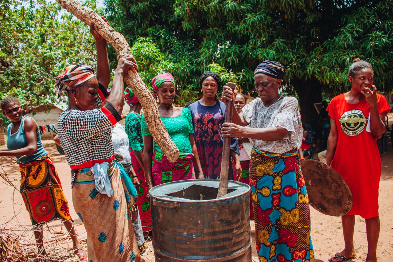services-01 Group of women in colorful traditional clothing cooking outdoors.