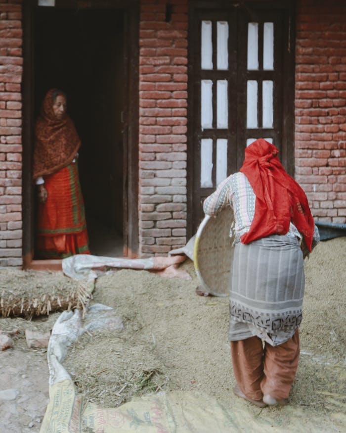 why-choose-us Women engaged in traditional work outside a rustic brick house in a rural village.