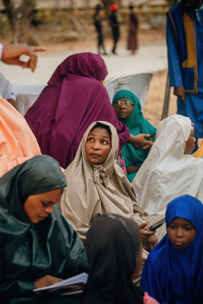 gallery-2 Women in colorful traditional attire participate in a community gathering outdoors.