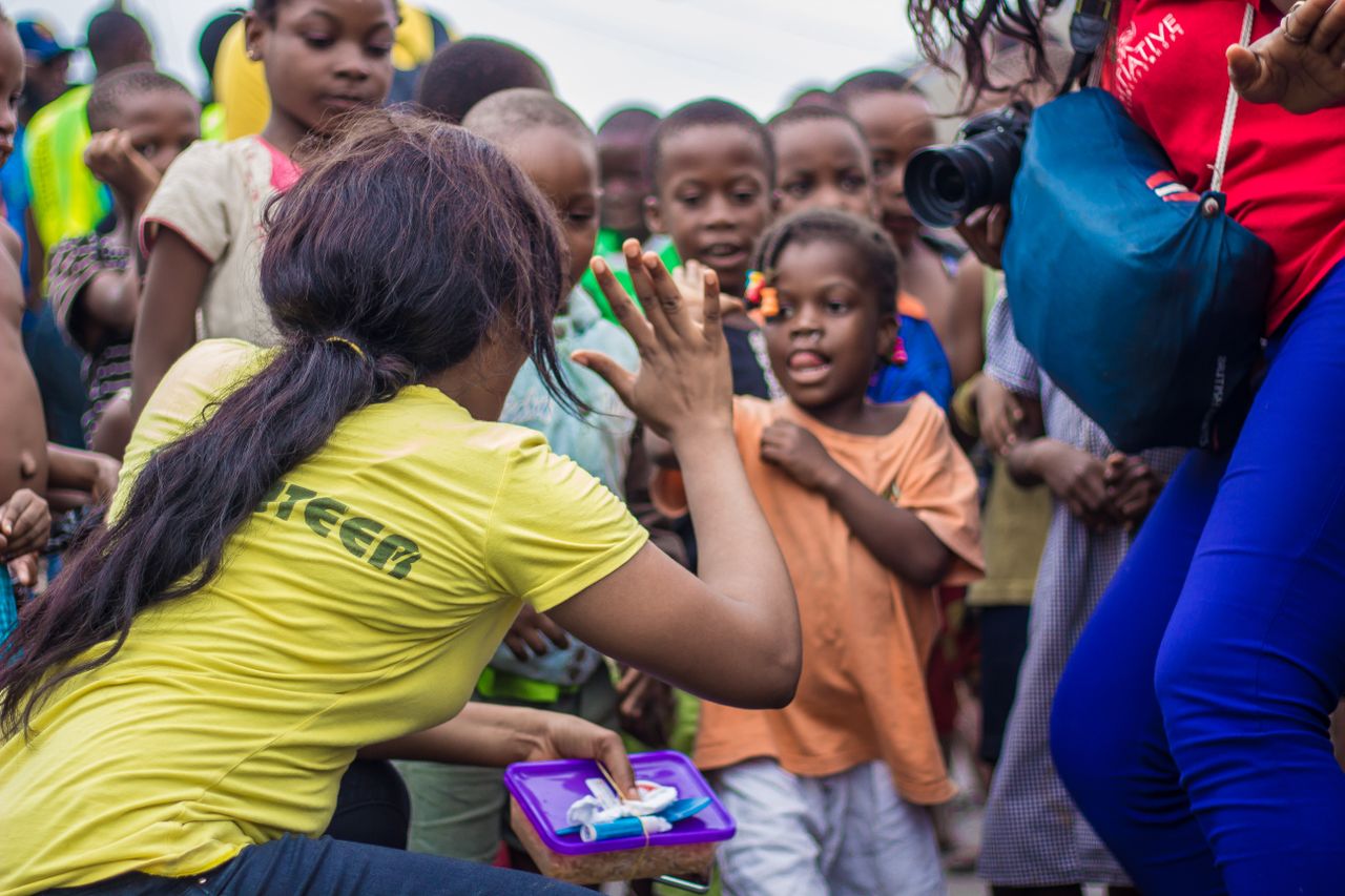 hero-img-02 A woman engages with children through a high-five in a vibrant community setting.